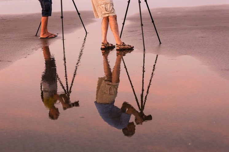 Reflection of two photographers using tripods on the beach