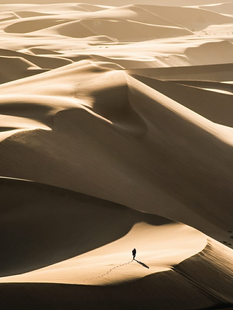 person walks on sand dunes with negative space above