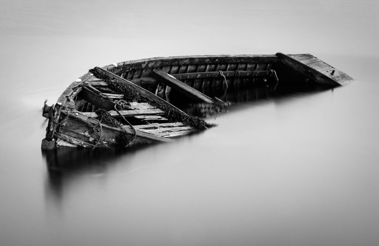 water around an abandoned boat looks smooth when a long exposure technique is used