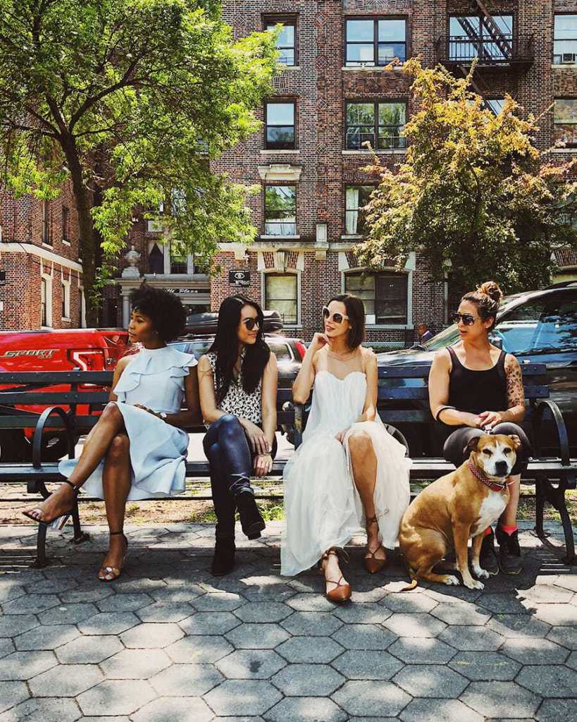 A sample photo of 4 women and a dog sitting on a distractive background consists of apartment blocks. Taken using a deeper DoF