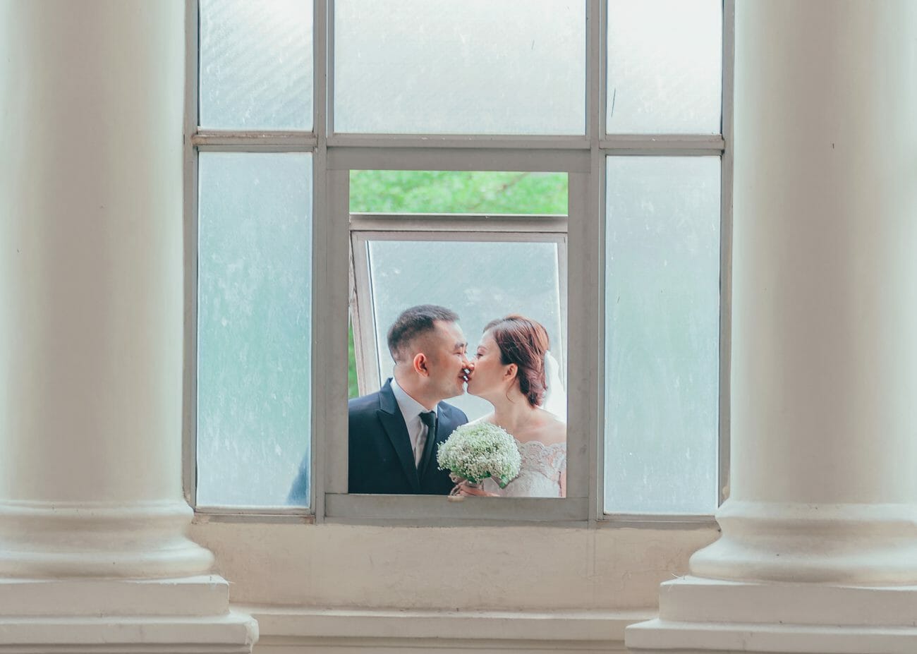 A bridge and groom kiss, framed by pillars and a window