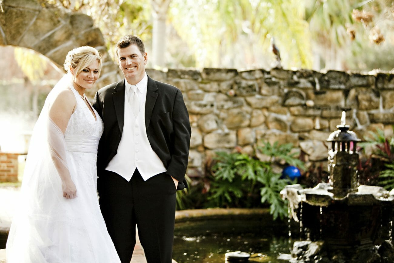 A smiling bride and groom together infant of  wall and lanterns, demonstrating one  of the classic wedding poses