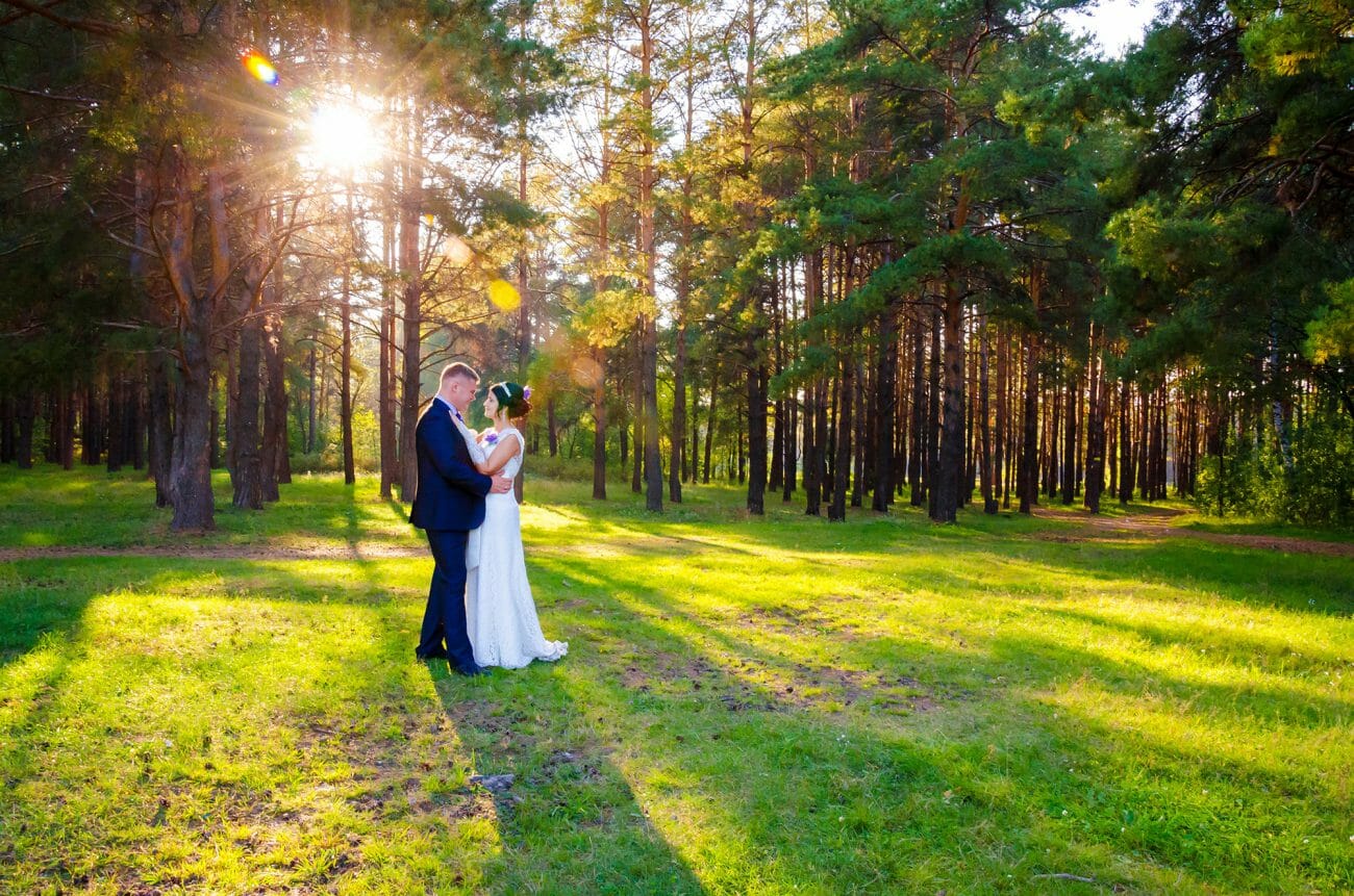 A bride and groom stare at each other infront of a woodland setting, with sun streaming through the trees