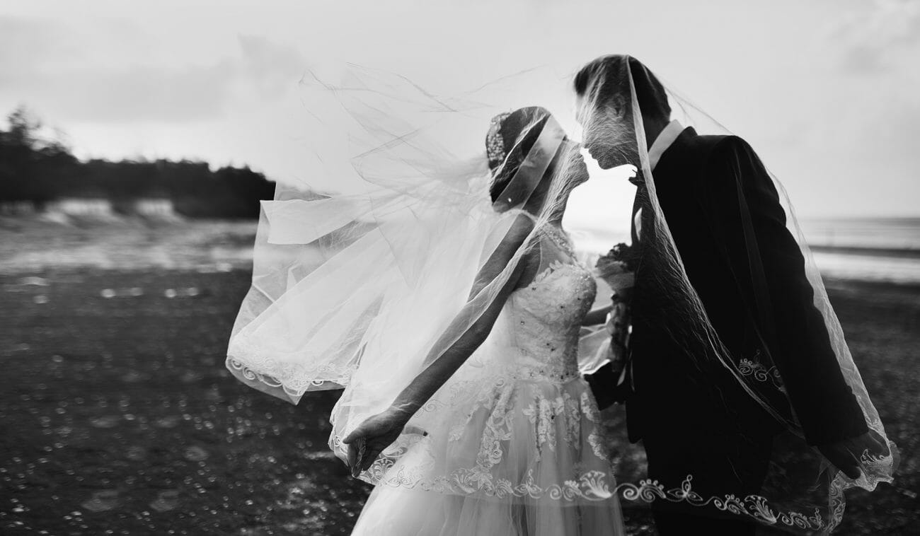 A black and white image of a couple about to kiss underneath the bride's veil