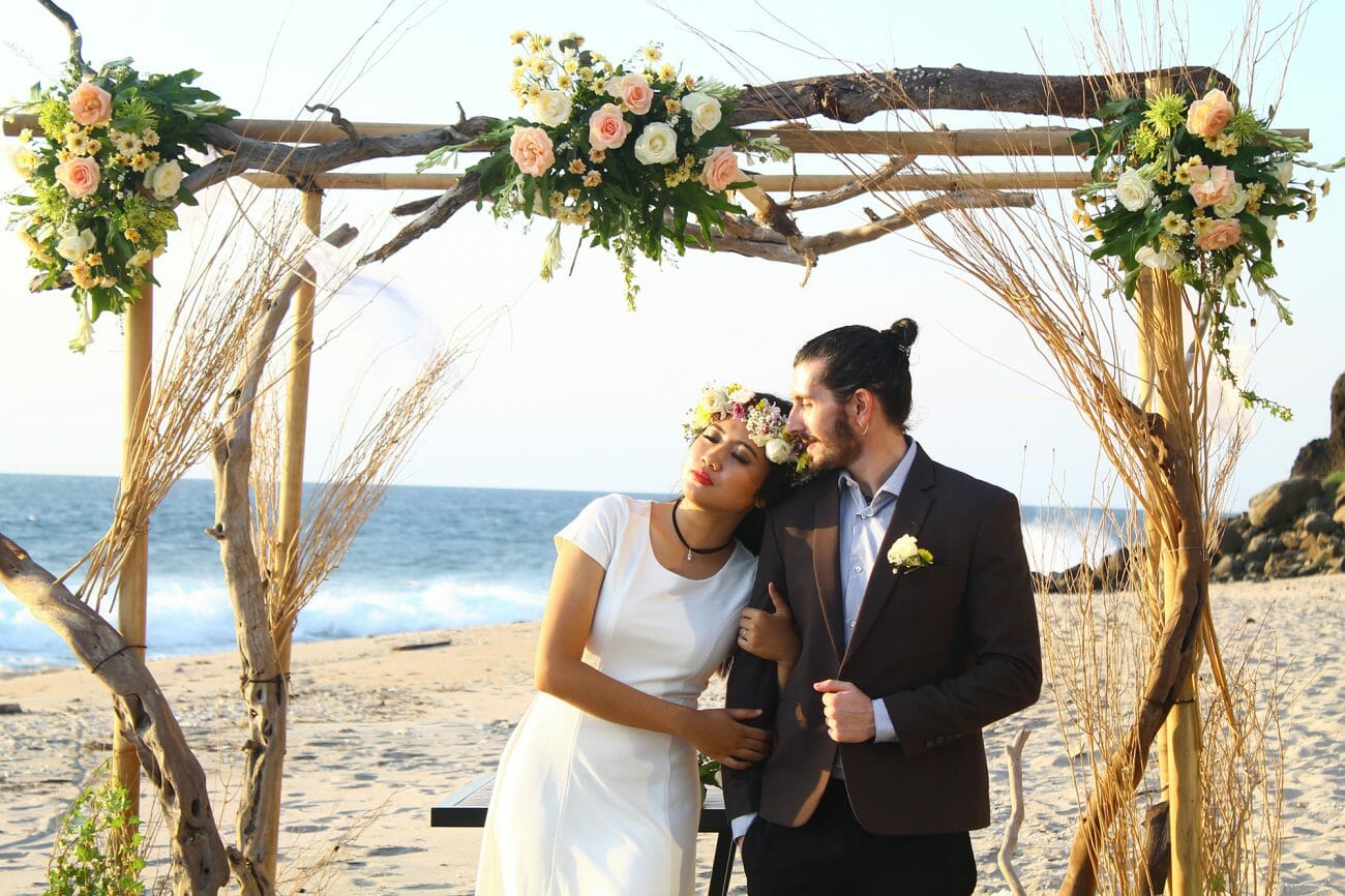 A bride and groom framed by a wooden archway and flowers