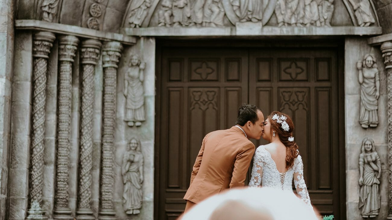 A wedding couple face each other, backs to the camera, framed by a beautiful church doorway