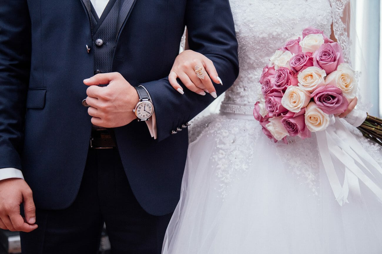 A middle body shot of a bride and groom arm in arm, the bride holding  bouquet