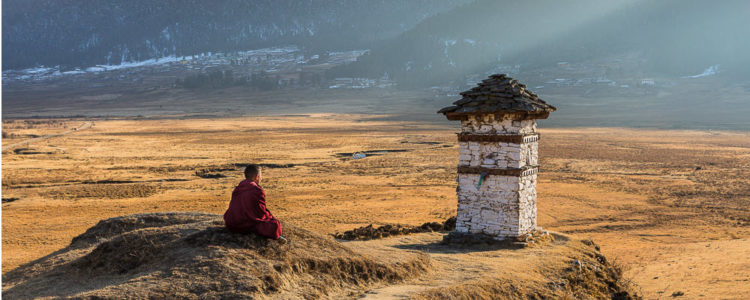 Bhutanese monk sits on a mound in a barren valley lit by the sun