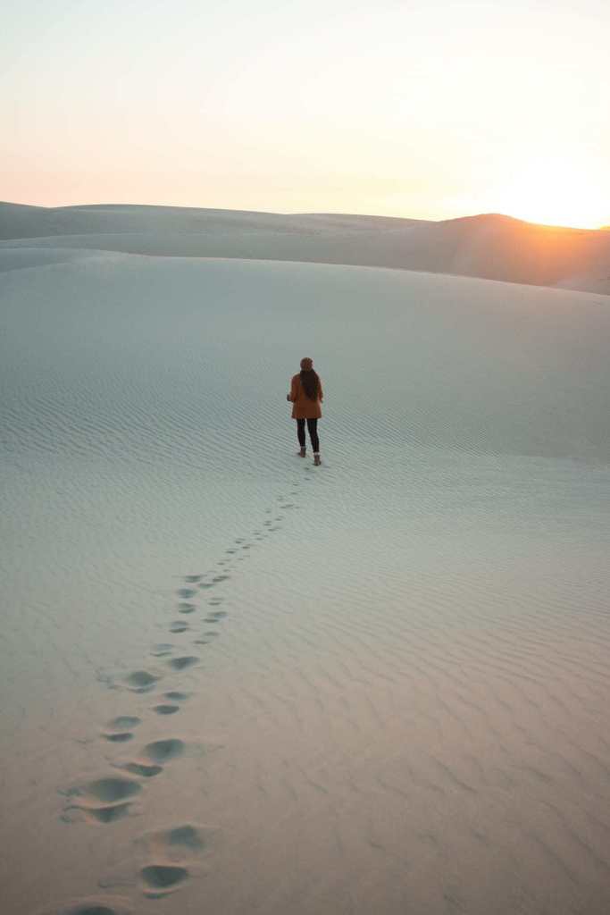 A women walking across sand dunes while her footsteps act as a leading line to compose the photo