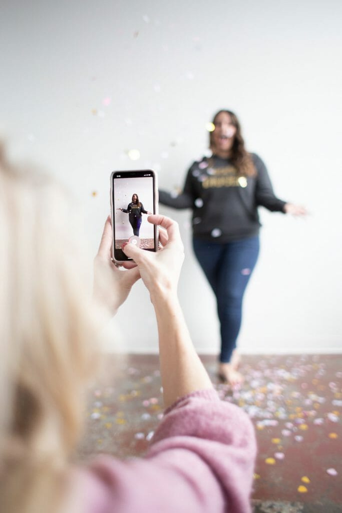 A photo of a woman throwing confetti in the air, viewed through the lens of a smartphone