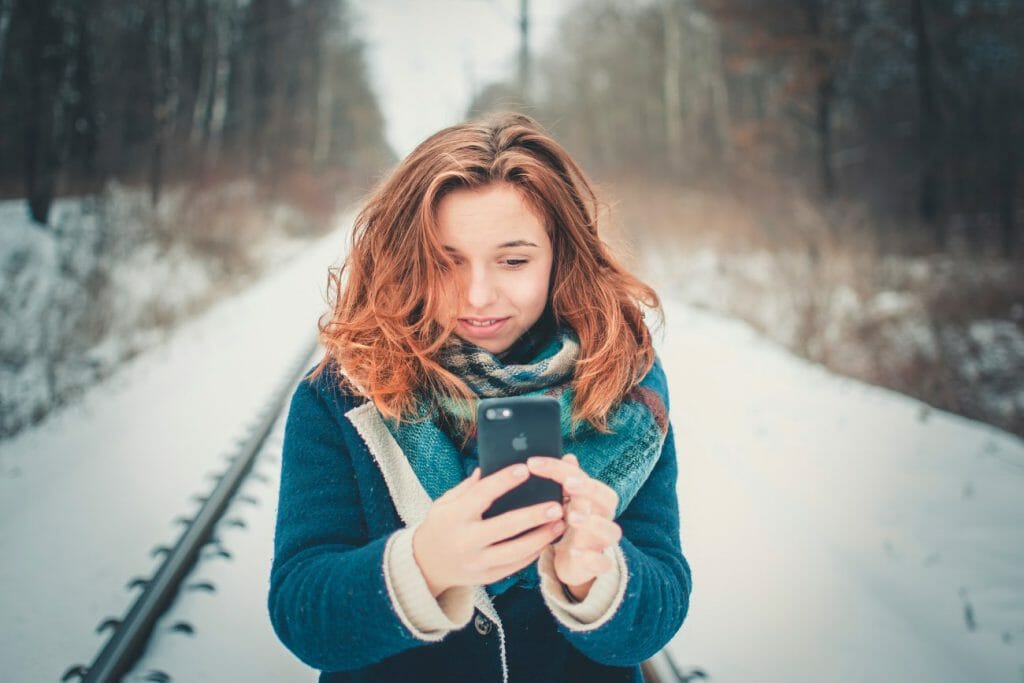 A girl in a wintry scene looking into her smartphone's front camera