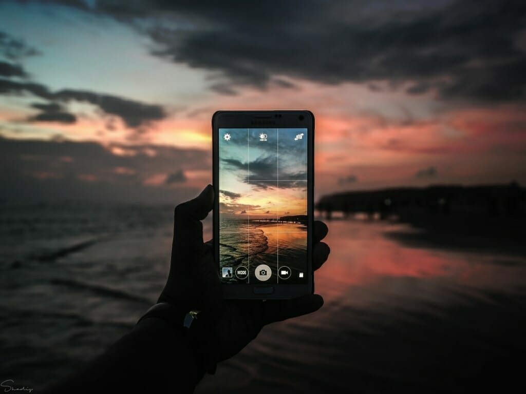 A photo of a sunset beach scene on the screen of a smartphone