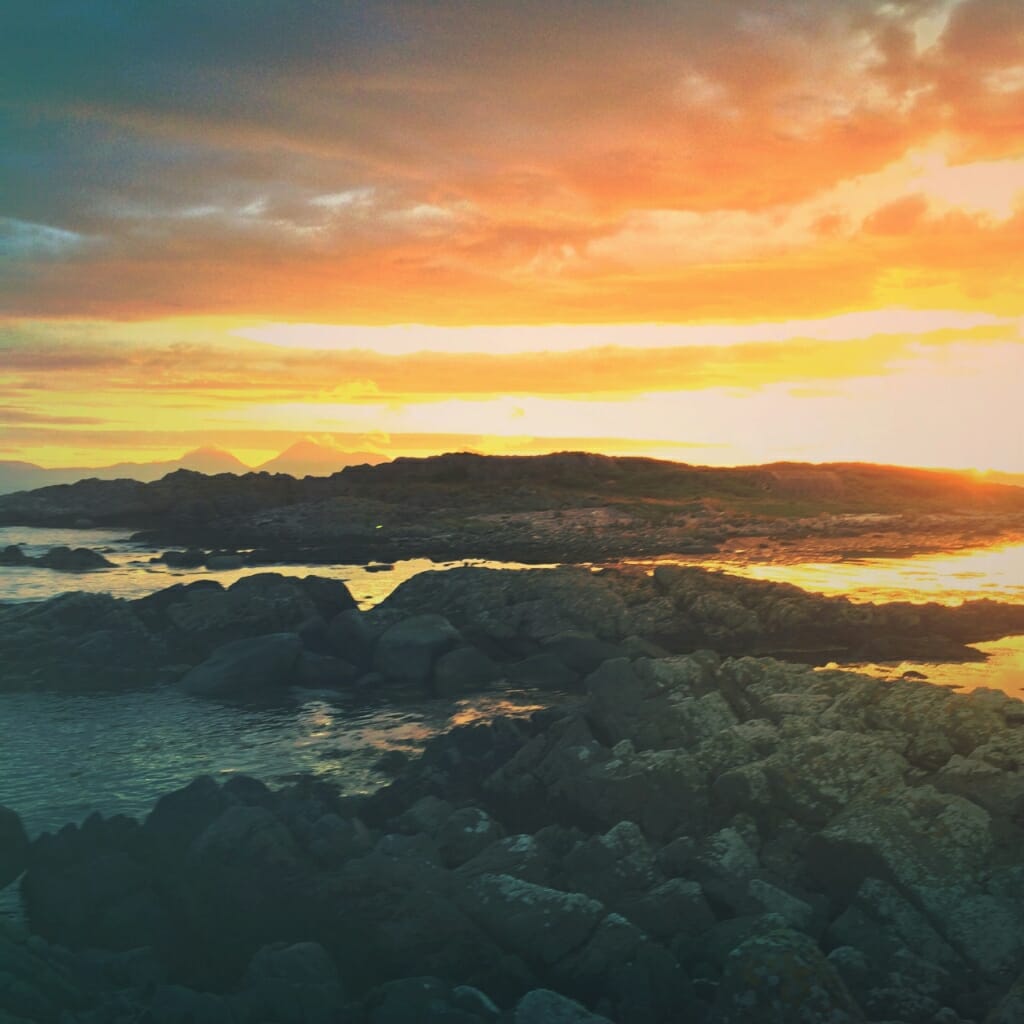 A mobile phone photo of a sunset over a rocky coastline