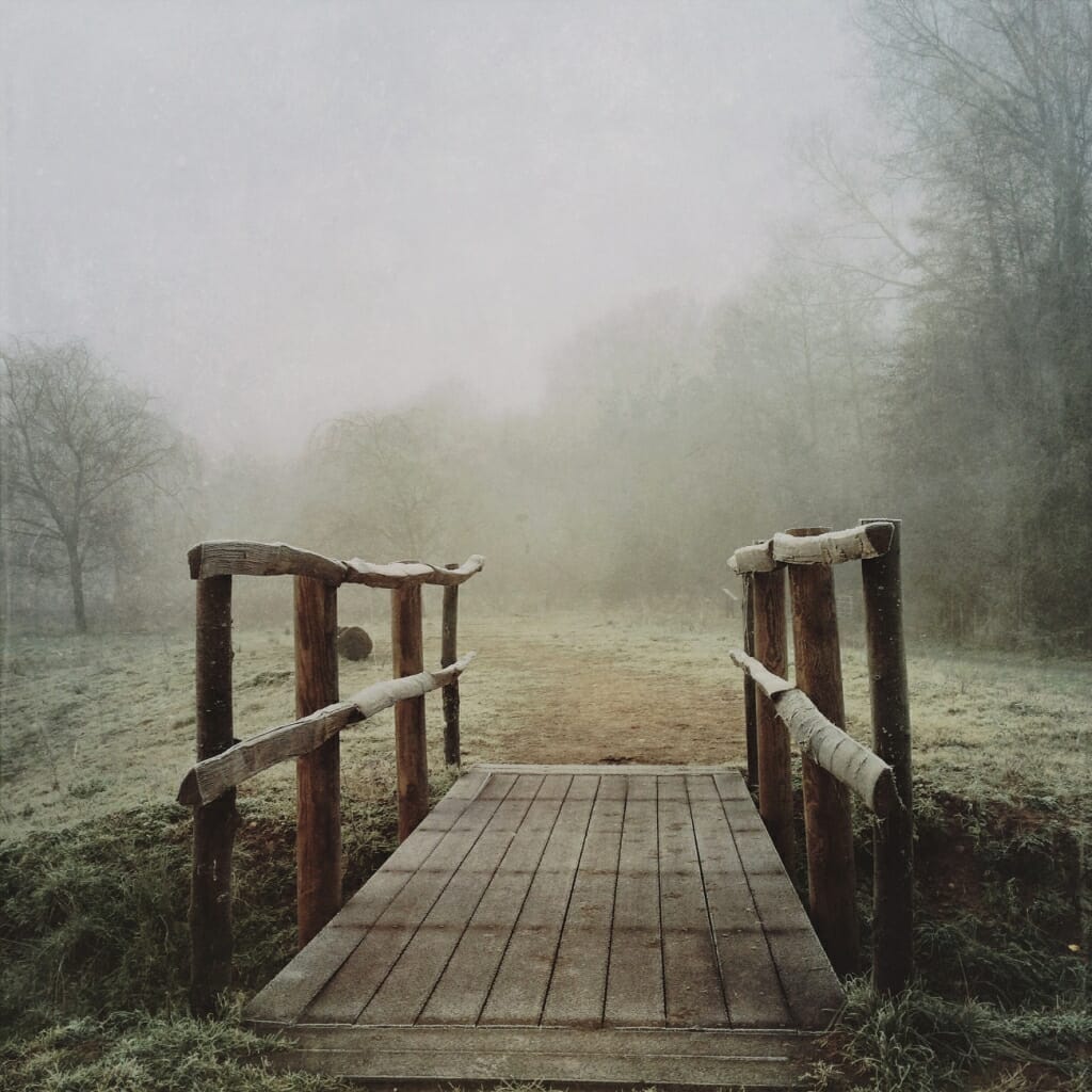 An iPhone winter shot of a bridge over a stream in a field