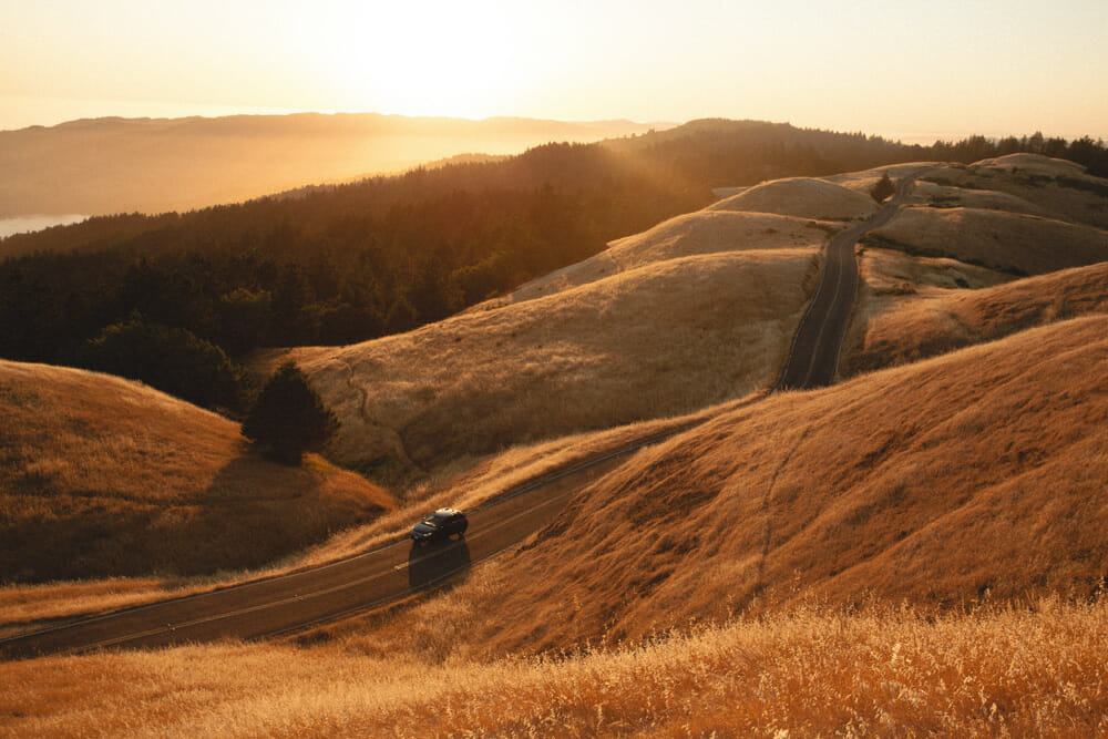 A car travelling through rolling hills at sunset