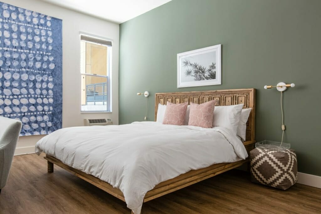 A wide interior photography shot at an angle of a bedroom with a wooden bed and a green wall