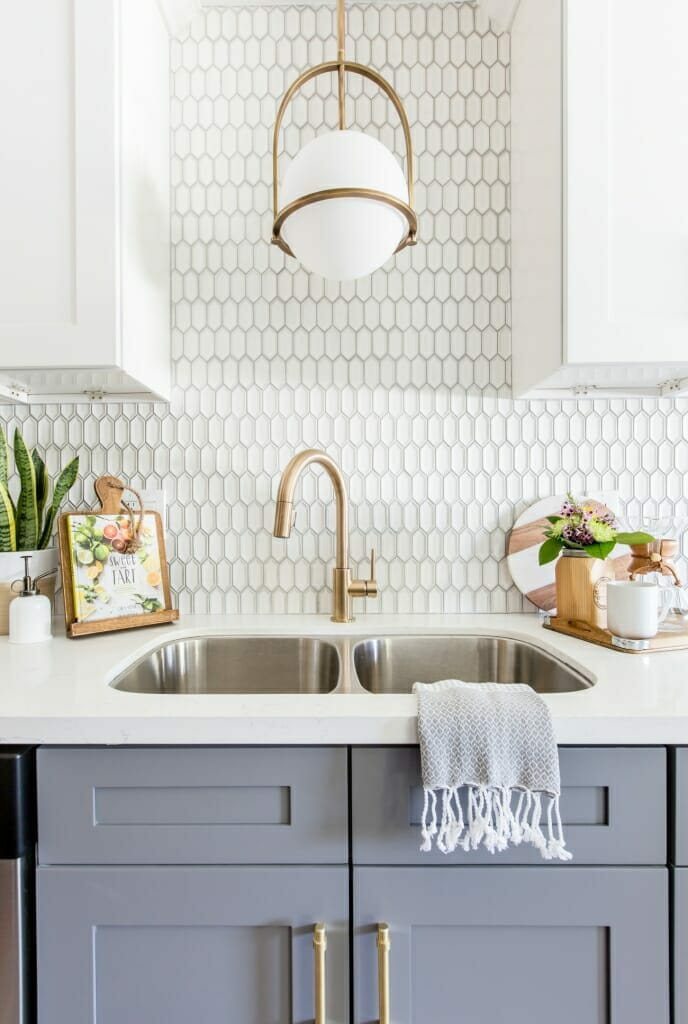 A vignette shot of a kitchen sink with a bronze tap and grey cabinet doors