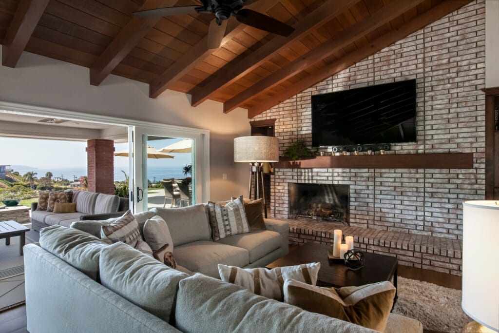 An interior photography shot of a spacious living room with a large, grey L-shaped sofa and wooden ceiling