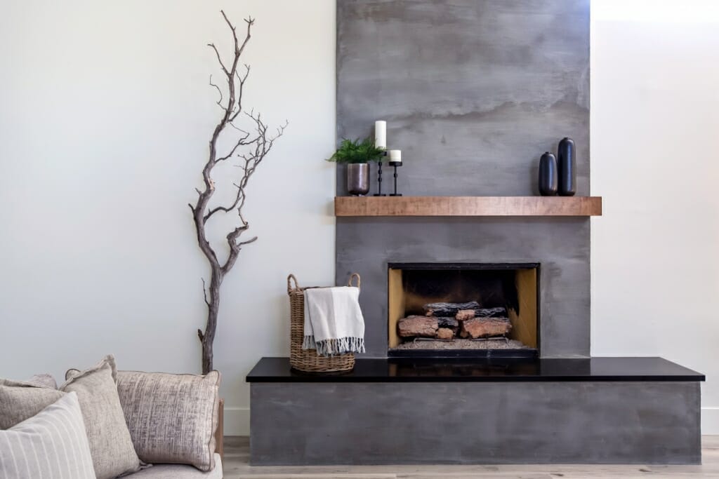 An image of a grey fireplace with a wooden shelf above it