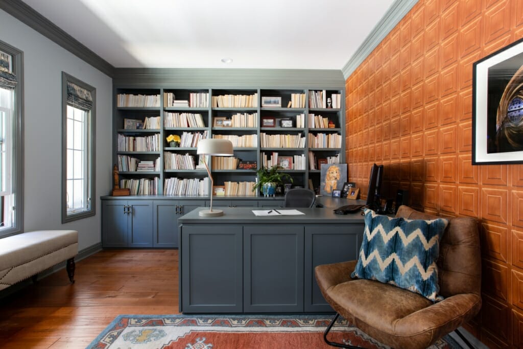 An image of an office space with a wall of bookshelves and a grey desk with a brown leather chair infant of it