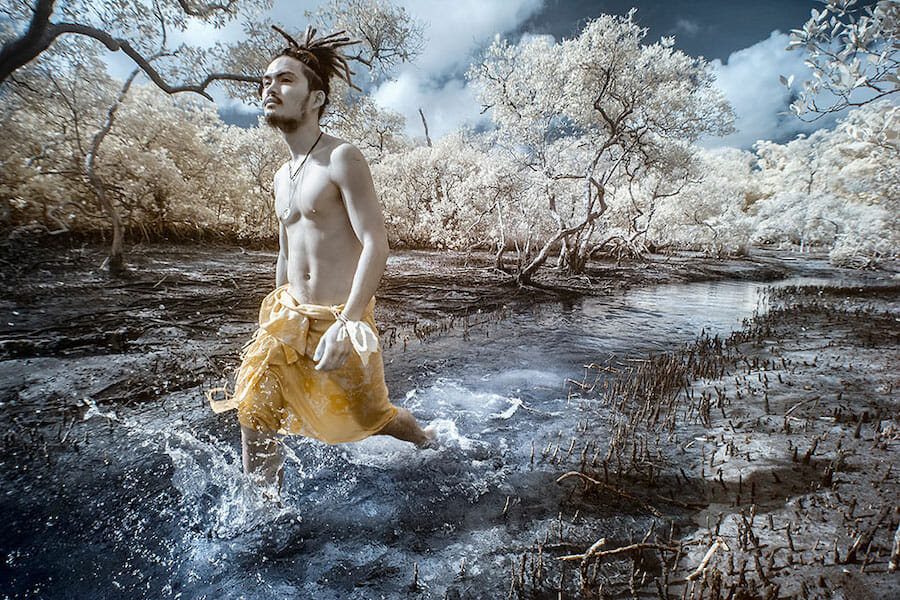 An infrared portrait photo of a man walking through a stream