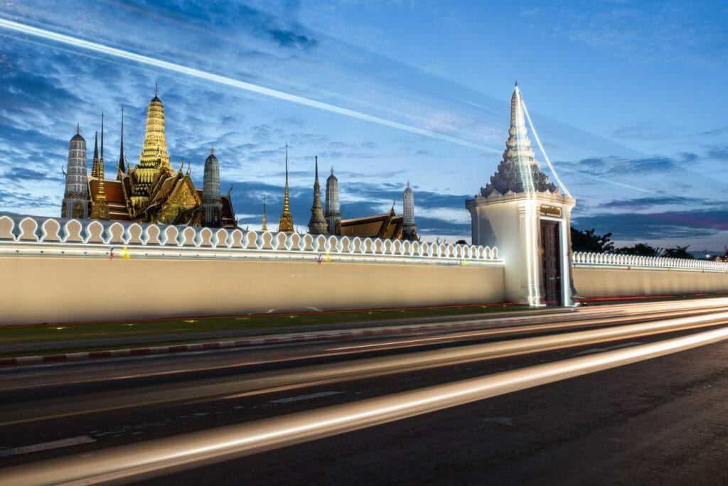 Motion blur light trails along a street frame a golden temple in Bangkok