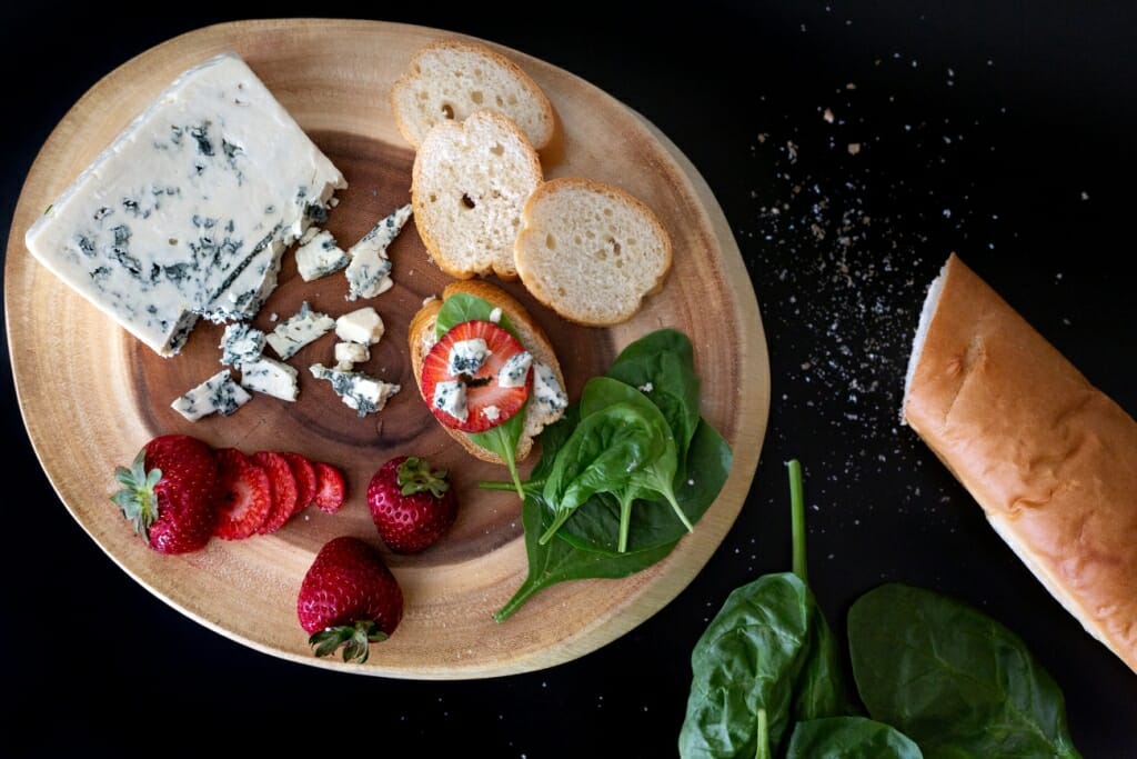 Bread, cheese, herbs and fruit on a wooden board on a black kitchen counter