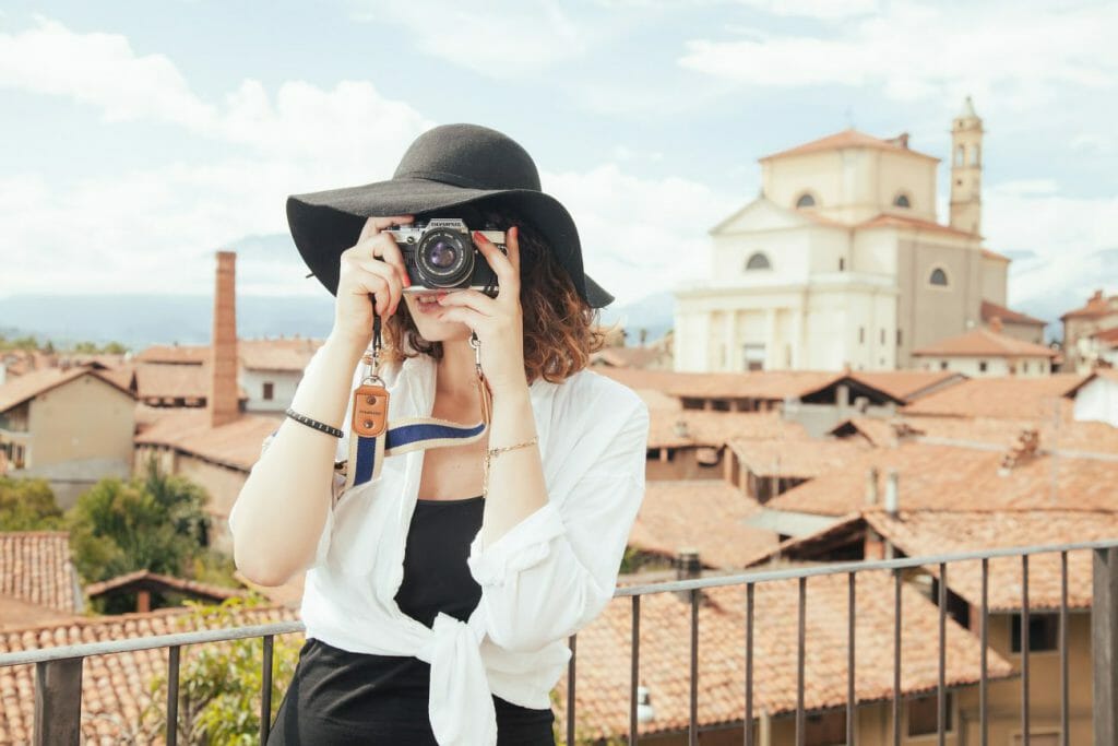 A photo of a woman in a hat taking a photograph with a camera