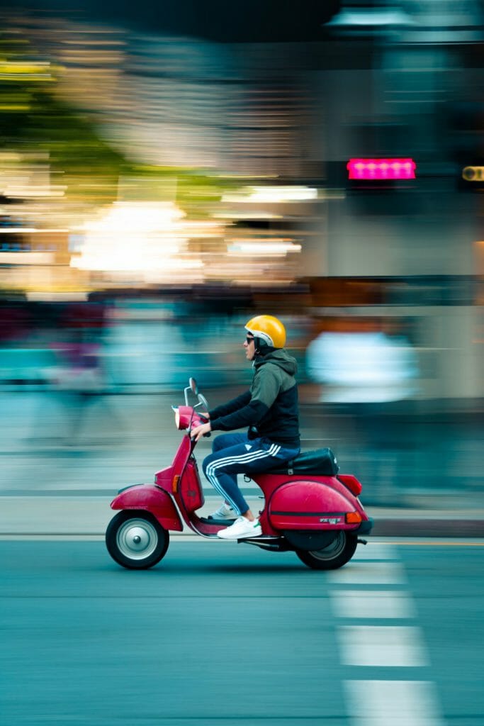 A panning photo of a moped traveling along a road