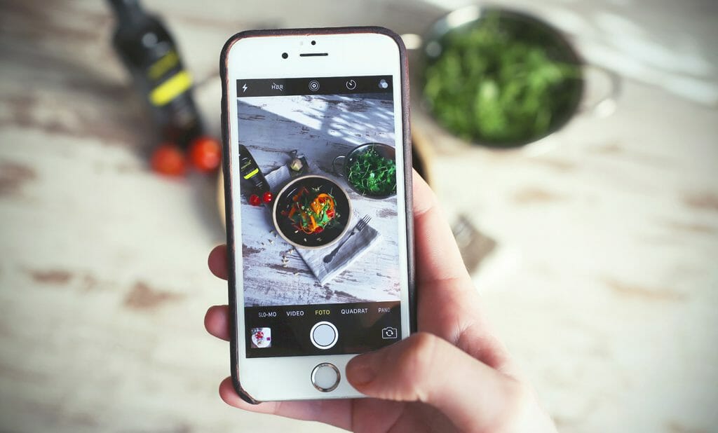 A person taking a photo with their smartphone of food laid out on a table