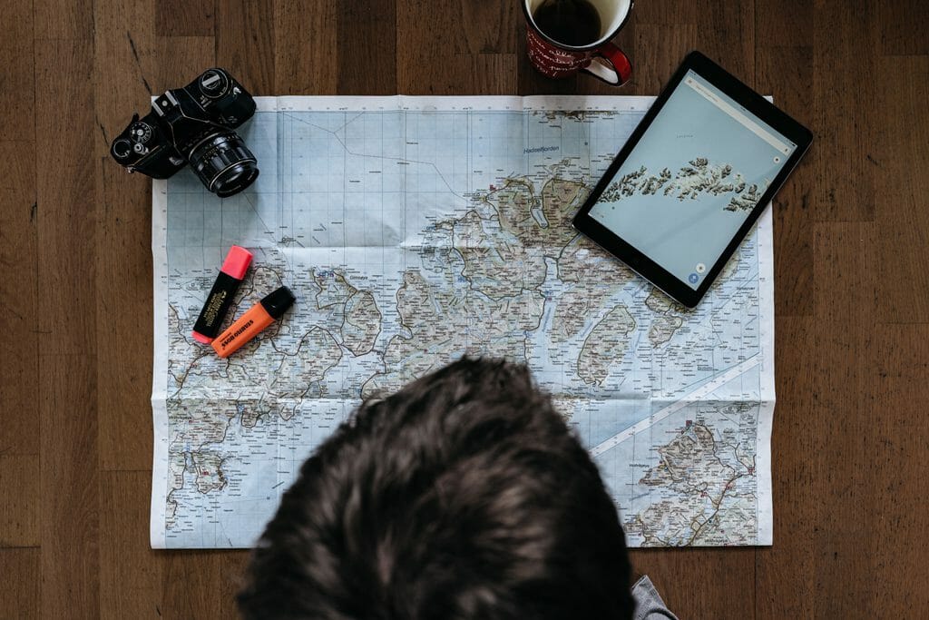 An image of a man looking at a map with a tablet, his camera and highlighter pens