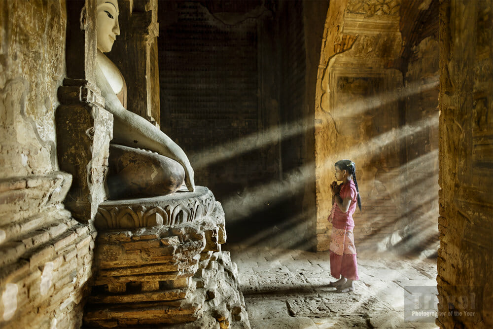 An image of a young girl praying in front of a Buddha statue