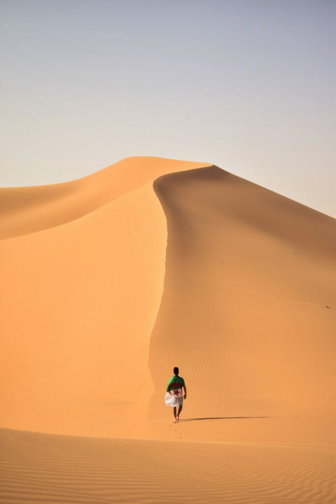 An image of a man walking towards a mountainous sand dune