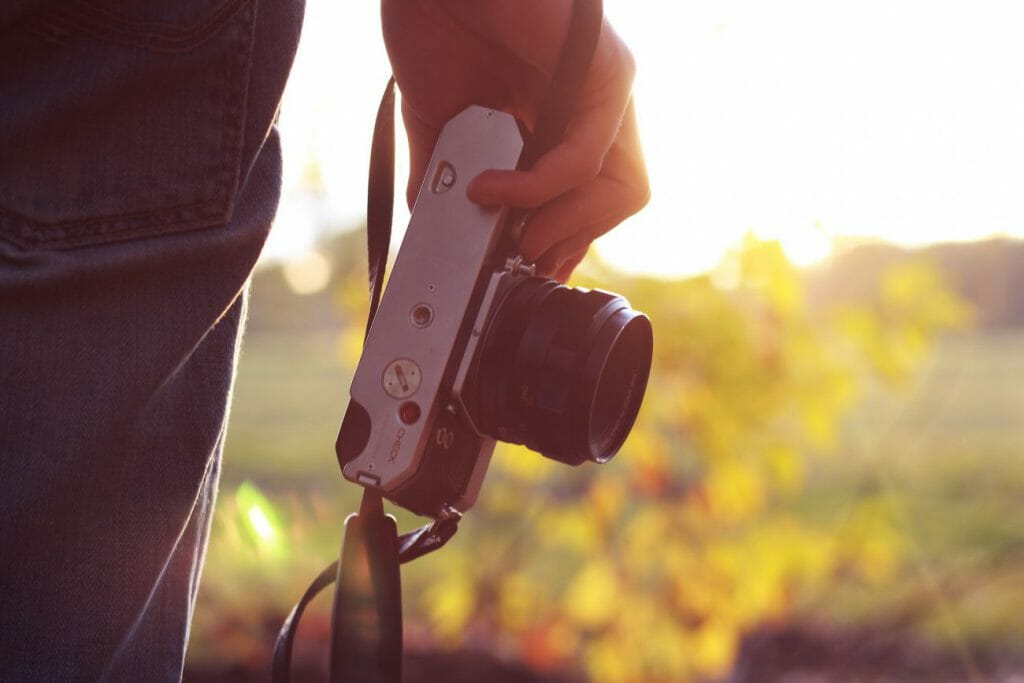 A photo of a man's hands holding a small camera in a field