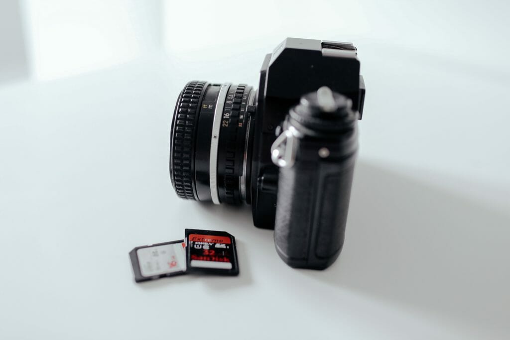 A camera sat on a white table tops next to 2 memory cards