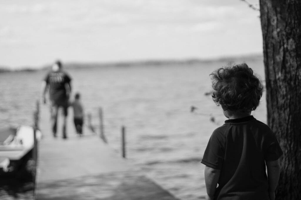 A child looking at a father and sibling walking on a pier. 