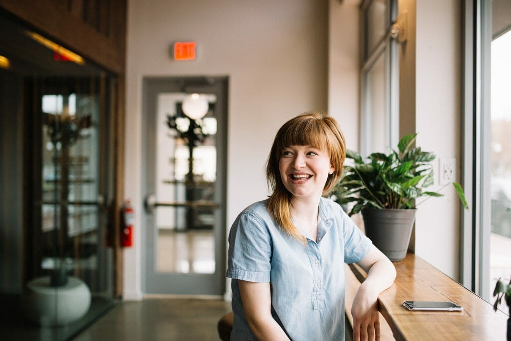 A smiling lady sat at a counter, lit by a large window in front of her