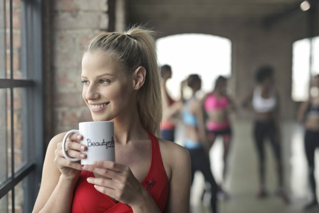 Indoor photography of a woman at the gym holds a mug while looking out of a window