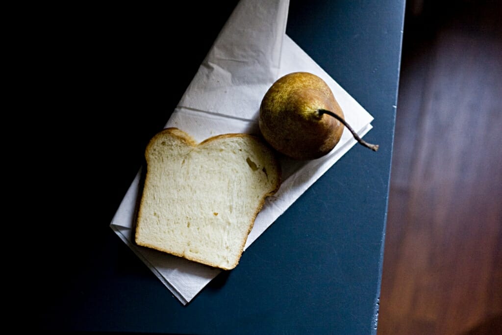 An indoor photography shot of a slice of bread and a pear sat on a napkin on a table