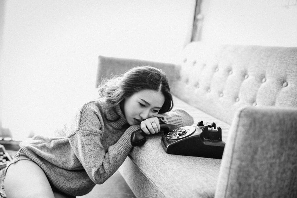 A girl leaning on a couch holding an old phone.