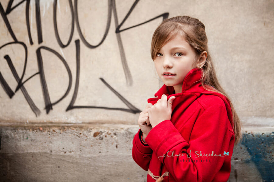 A girl in a red duffel coat in front of a wall of graffiti