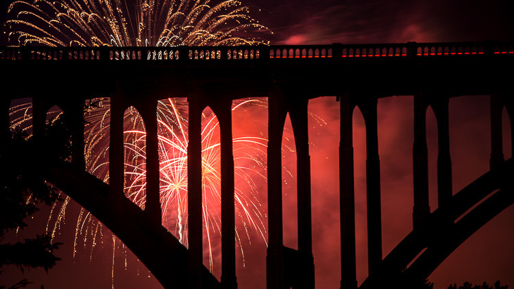 Bridge silhouette captured with red glow from fireworks exploding behind it by zooming in tigher