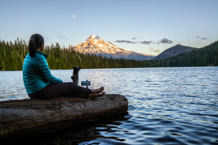 Woman sitting on a log photographing a mountain with her phone