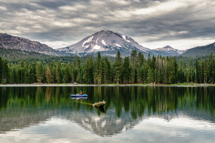 Mountains of Lassen Volcanic National Park with a fisherman in a boat pictured in the foreground, adding a human element