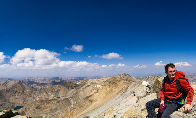 mountain range panoramic photo with a hiker sitting which adds a human element