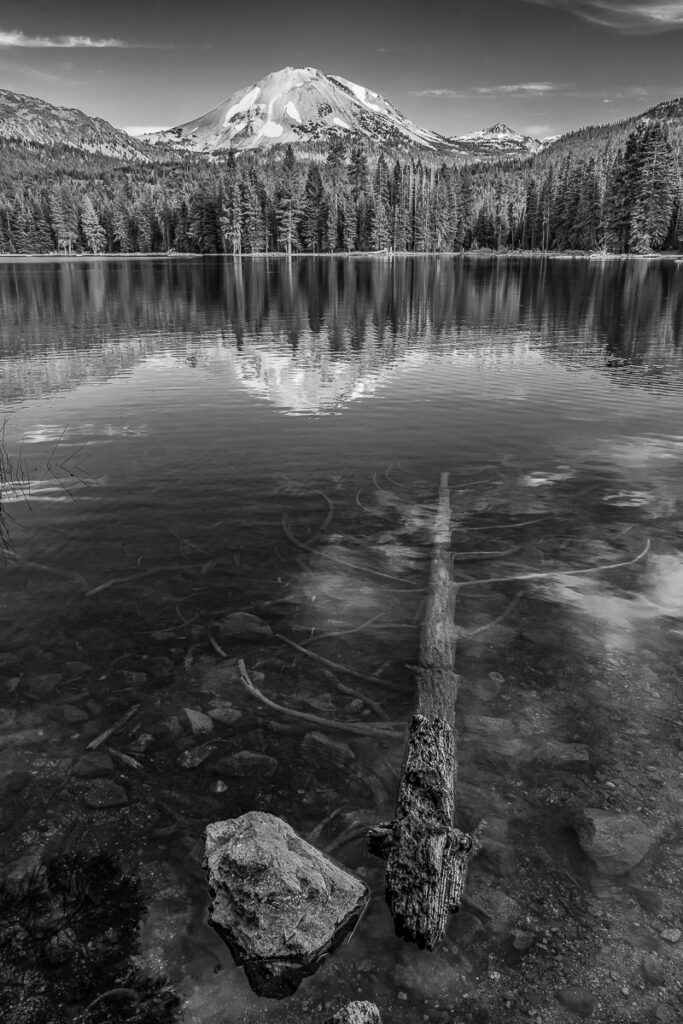 portrait orientation photograph in black and white of a lake, trees and mountains behind