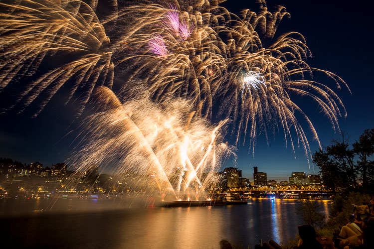 Fireworks captured bursting and streaking over water with city and bridge ISO 100, f/8, 8 seconds