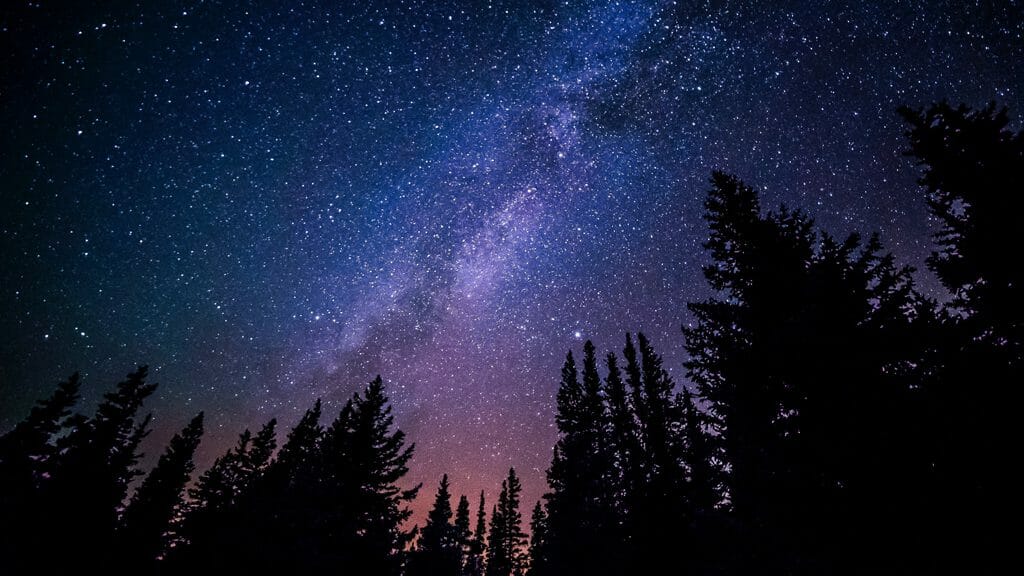 A colorful night shot of the Milky Way over silhouetted trees