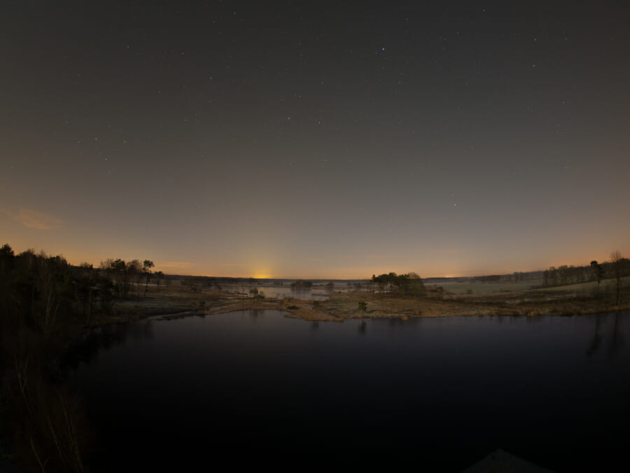 A night shot of a Belgian landscape showing orange light pollution on the skyline